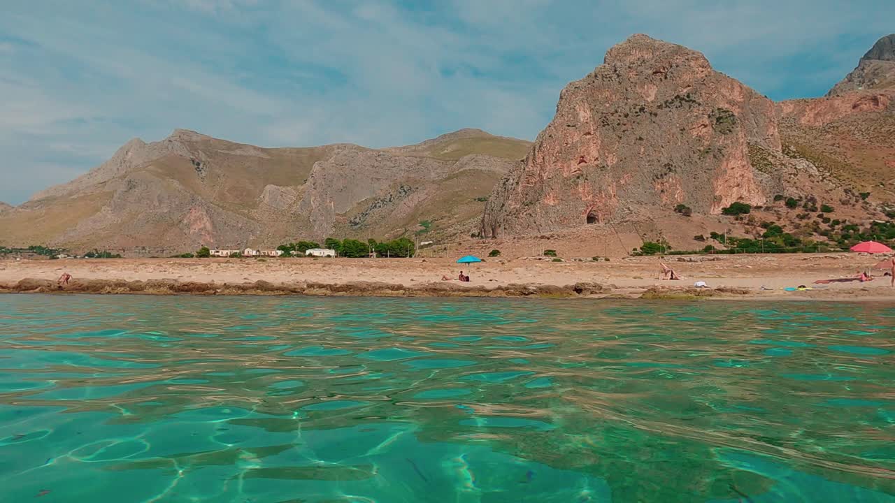 Hot summer day at Baia Santa Margherita and surrounding landscape in Sicily with people bathing in turquoise sea water