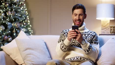 Portrait-Of-Joyful-Young-Man-Smiling-With-Surprised-Face-Tapping-On-Cell-Phone-Feeling-Excited-And-Happy-Winning-Christmas-Lottery