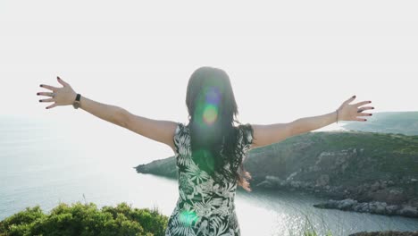 a young girl opening her arms on the top of the hill against the stunning view and sun