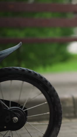 a young boy is seen from the legs down, as he approaches and climbs onto a bicycle, wearing denim shorts and colorful sandals, the child rides off with the bicycle on a paved path