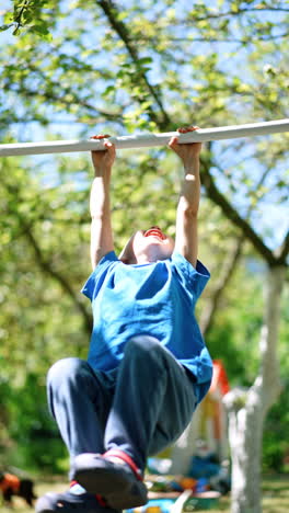 smiling caucasian boy stands outdoors holding hands on the horizontal bar. kid rises feet and waves on the bar. vertical video.