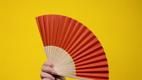 A-hand-holding-and-shaking-red-paper-fan-to-create-a-gentle-refreshing-wind