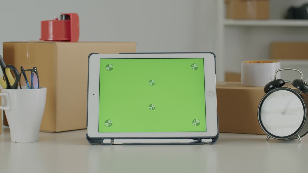 tableta con una plantilla de pantalla verde en blanco en la mesa y con fondos de cajas de paquetes en la oficina en casa.