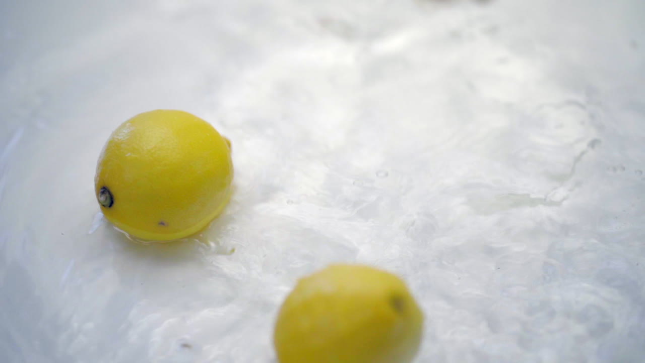 SLOMO of Lemons Falling into Water on White Backdrop