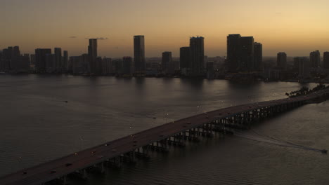 Miami-Bridge-Mit-Vorbeifahrenden-Autos-Und-Der-Innenstadt-Von-Miami-Im-Hintergrund-Bei-Sonnenuntergang.-Luftaufnahme