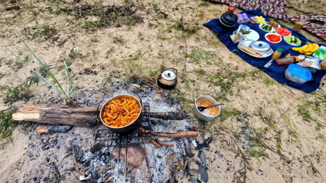 food cooking over a fire pit with a picnic spread on sand nearby. tallinn, estonia