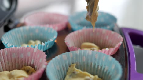 close up of adding cake mixture to paper cupcake baking tray