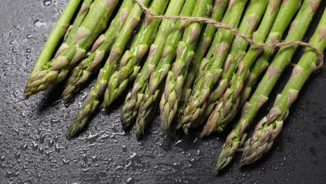 raw green asparagus on wet black slate background