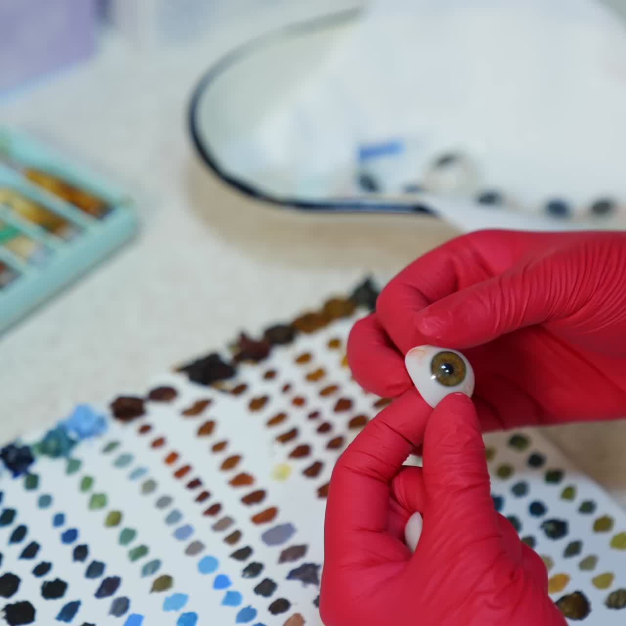 Artificial eye in doctor's hands. Medical specialist in latex gloves holding eye prosthesis on paints background
