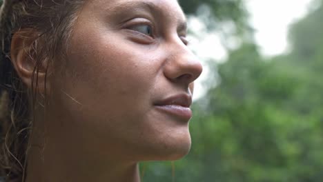 a close-up portrait of a woman with a genuine smile and wet hair, looking up and to the side, with the blurred green foliage of rio celeste's rainforest in the background