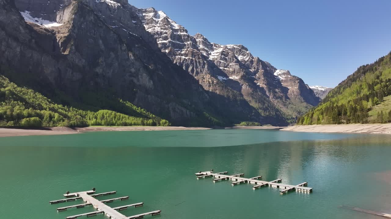 Aerial Klöntalersee lake with docks and snow capped peaks in Glarus Switzerland