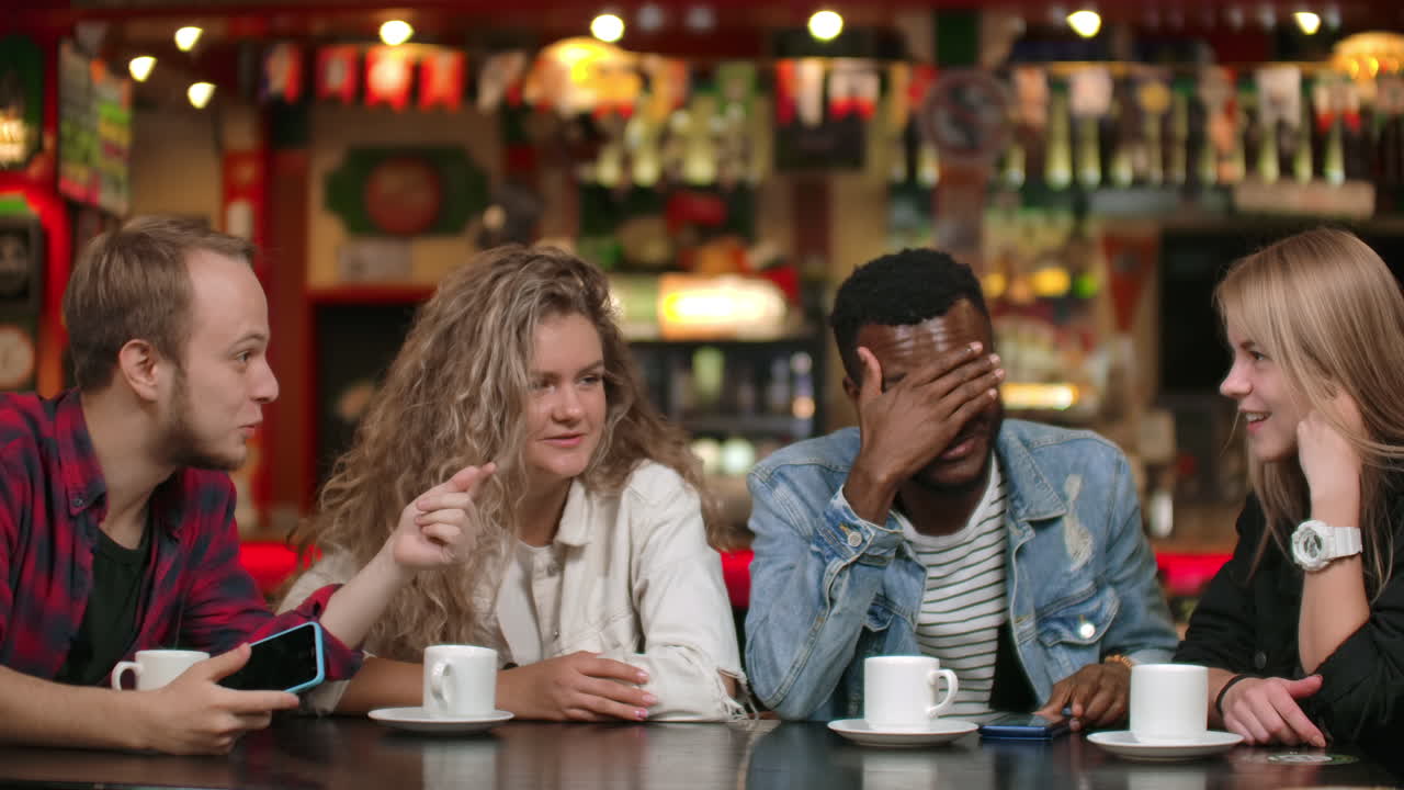 Multinational group of man and woman sitting together at a table with cups of coffee smiling laughing and telling emotionally and gesturing stories.