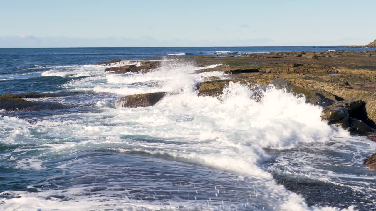 Slow motion landscape of ocean waves swell crashing onto rocky boulder seaweed reef formations along headland coastline near Bateau Bay town suburbs Central Coast Australia tourism travel destination