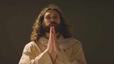 retrato de un hombre con cabello largo y barba que representa la figura de jesucristo poniendo las manos juntas en oración