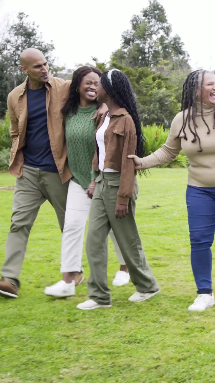 Vertical video: Starting walk, family holding hands, laughing across park, mom sweater, dad sliding