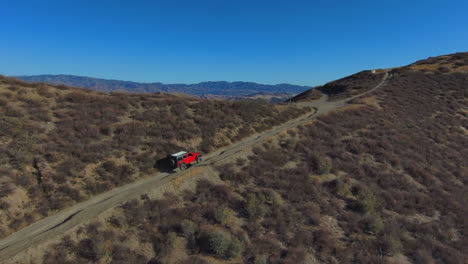 Epic-aerial-view-of-red-jeep-climbing-steep-hill-in-California-brusland-desert