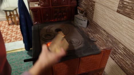 female adds pieces of wood into a traditional wood stove inside the house