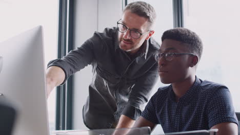 Two-male-colleagues-in-discussion-at-a-computer-monitor-in-a-creative-office,-low-angle,-close-up