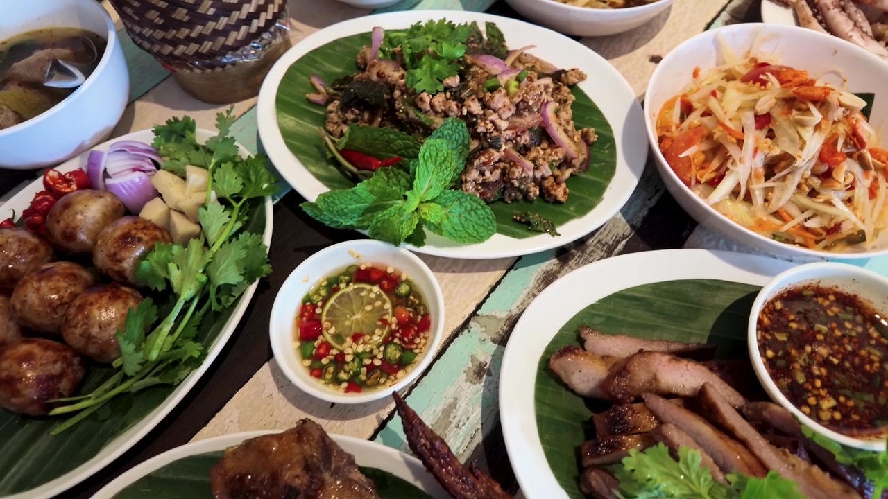 Pemandangan dari atas meja makan malam Thailand yang beragam, menampilkan salad pedas dan daging panggang.