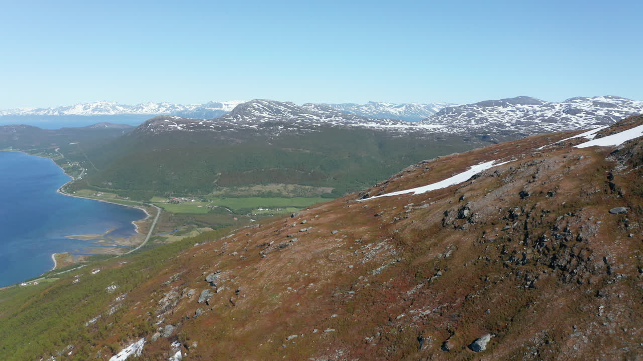 vista aérea sobre una montaña, revelando un pueblo en un valle, en la orilla del océano ártico, soleado, día de verano, en rotsund, troms, nordland, noruega - dolly, drone shot