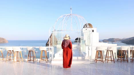 La-Parte-Trasera-De-Una-Mujer-Musulmana-Con-Vestido-Naranja-Y-Sombrero-De-Playa-Se-Está-Alejando,-Bajo-El-Cielo-Azul