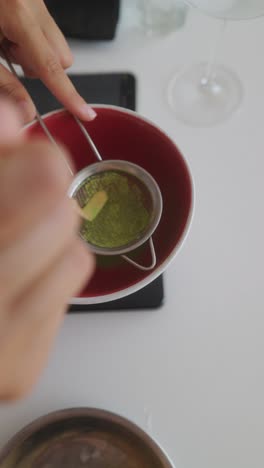 sifting matcha powder into a red bowl