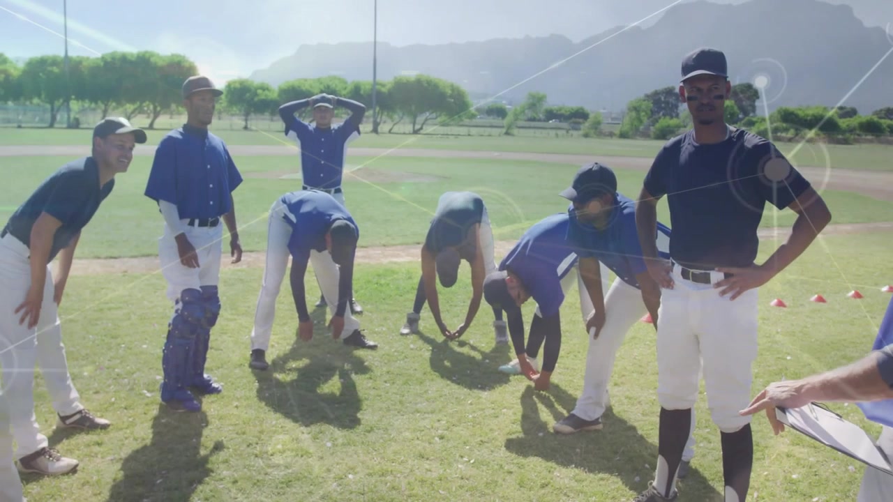 Allenatore di baseball che segnala il riscaldamento sportivo sul campo mentre i giocatori flettono i muscoli posteriori della coscia e prendono appunti.