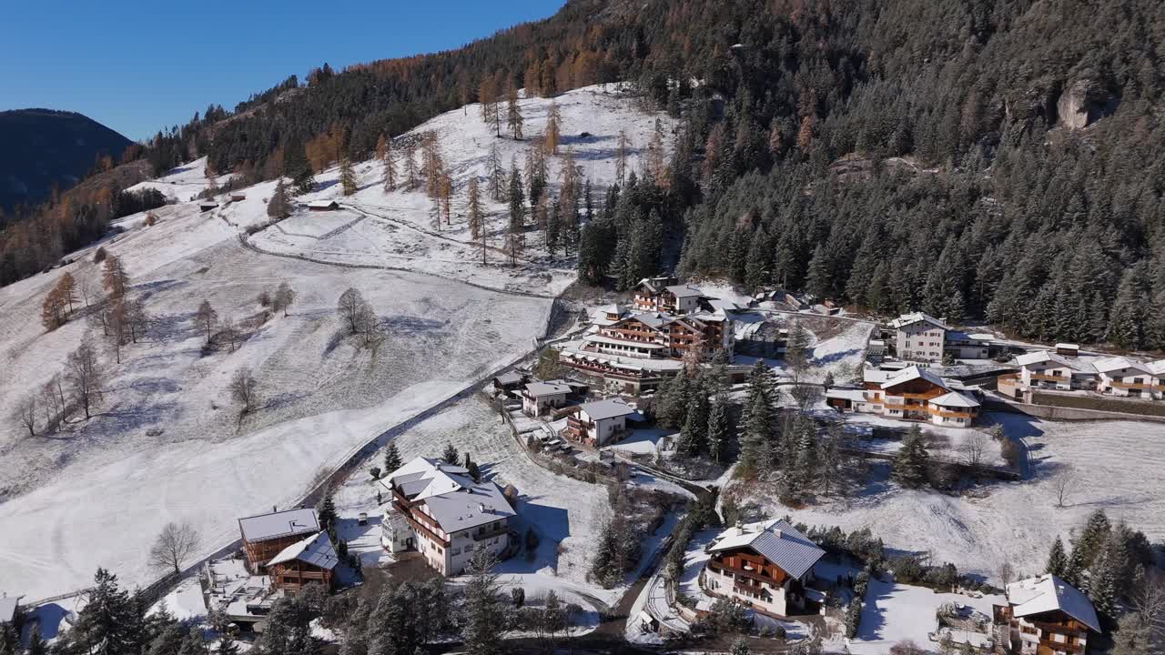 Detailed drone shot of the snowy alpine village Weißlahnbad near Tiers Tires in South Tyrol Alto Adige Italy with mountain homes snowy meadows and forest rising behind the houses