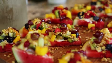 panning shot over slices of watermelon with a yogurt cream on top along with granola and a variety of fruits including blueberries, pineapple, strawberries, and raspberries