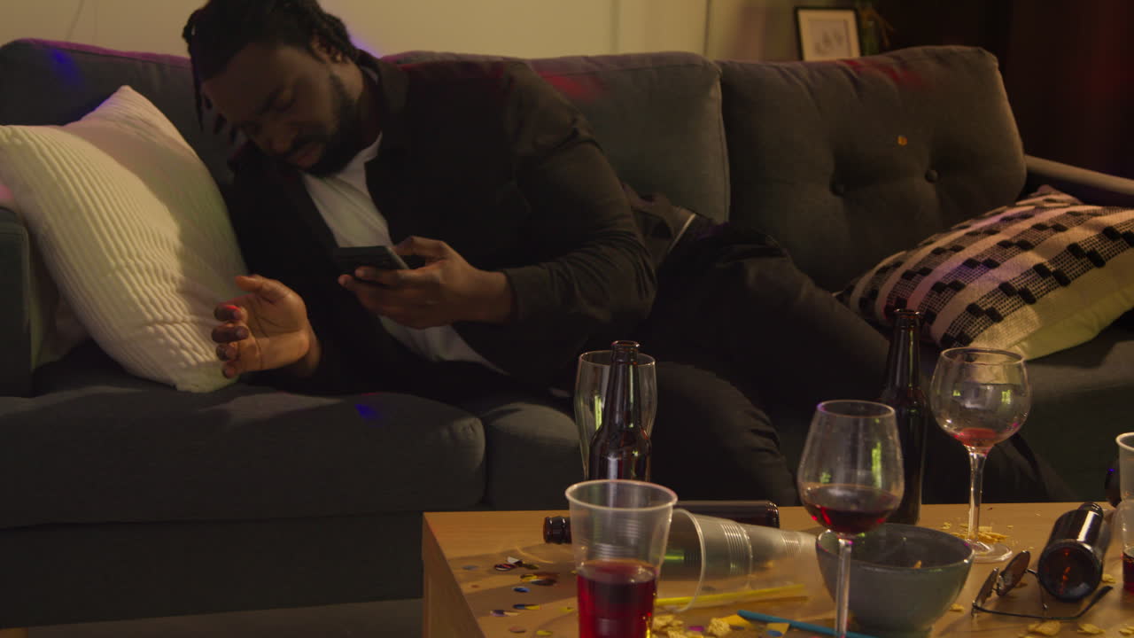 hombre despertando en el sofá después de beber alcohol en la fiesta de la casa sufriendo de resaca mensajería en el teléfono móvil