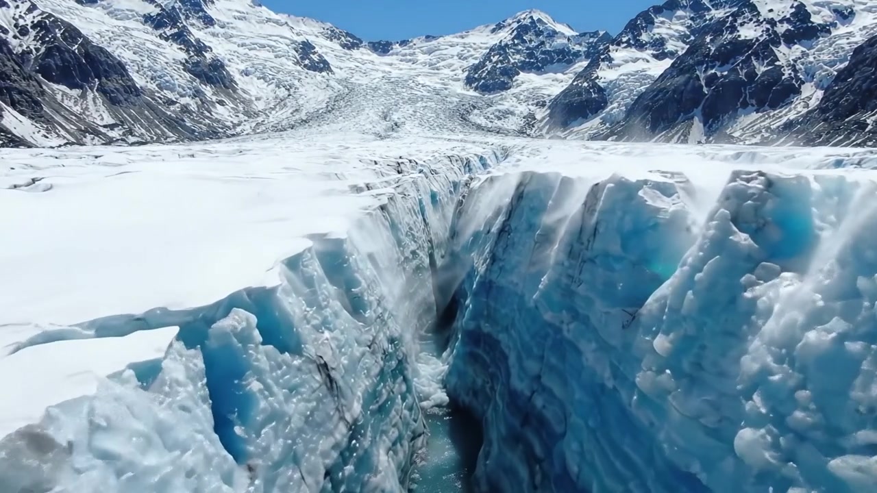 Vista aerea di un maestoso crepaccio glaciale che cattura le magnifiche formazioni di ghiaccio e le fessure nel paesaggio innevato sotto un cielo blu brillante.