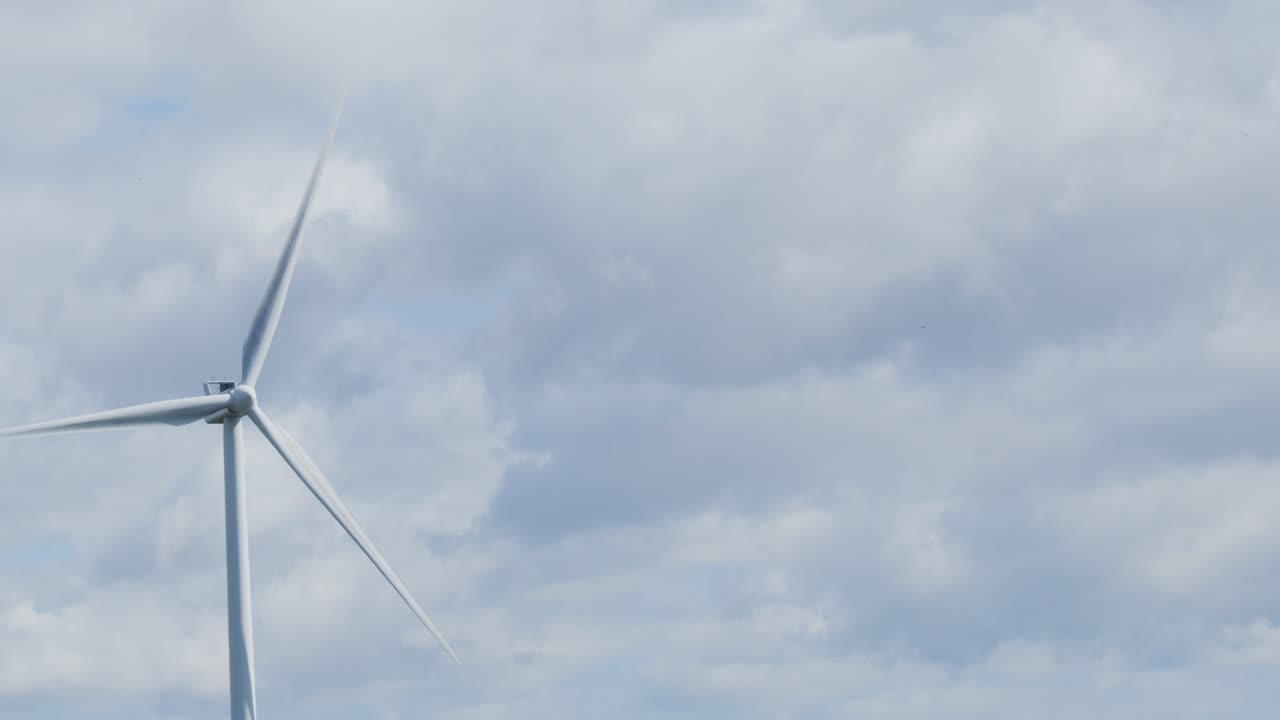 A single wind turbine slowly rotates under overcast skies in Edinburgh, Scotland. Static wide shot, natural daylight, calm and clean energy atmosphere