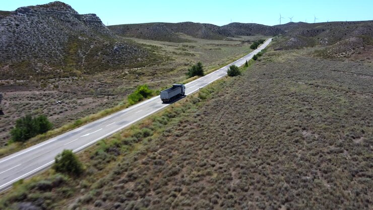 vista aerea di un camion in viaggio lungo il deserto, con mulini a vento sullo sfondo