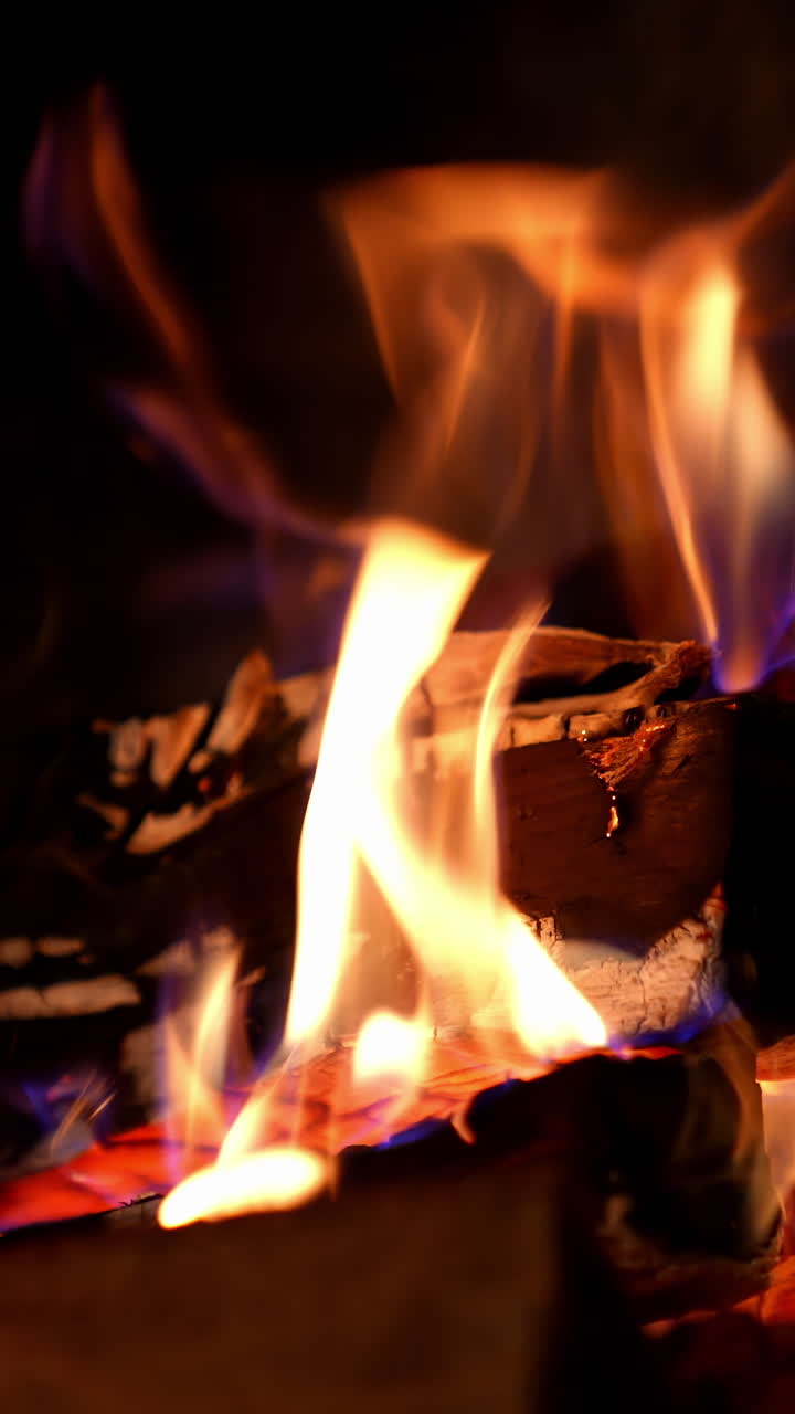 Cropped view of the wood burning in a fireplace during the night. Warm cozy fire in a fireplace. Autumn and winter holidays. Home cosiness concept. Vertical video