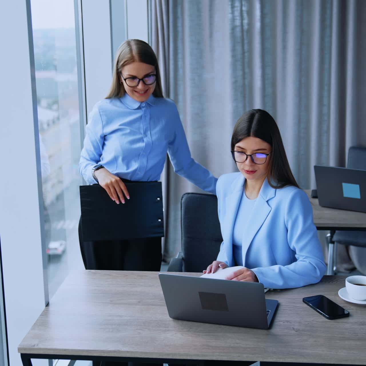 Blonde and dark-haired female employees having conversation in office. Business women look at laptop on the desk discussing some job issues