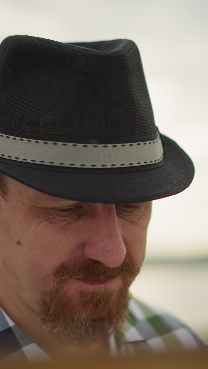 검은 모자와 초록색 체커 셔츠를 입은 남자의 클로즈업, 눈에 보이지 않는 작업에 깊이 집중하고, 머리 주변에 모기가 보인다.