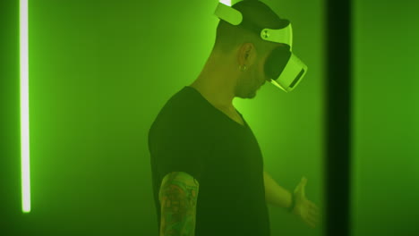 amazed guy exploring virtual reality near colorful lamps pan around view of astonished man in vr glasses moving hands and interacting with virtual reality while standing amidst multicolored neon lamps