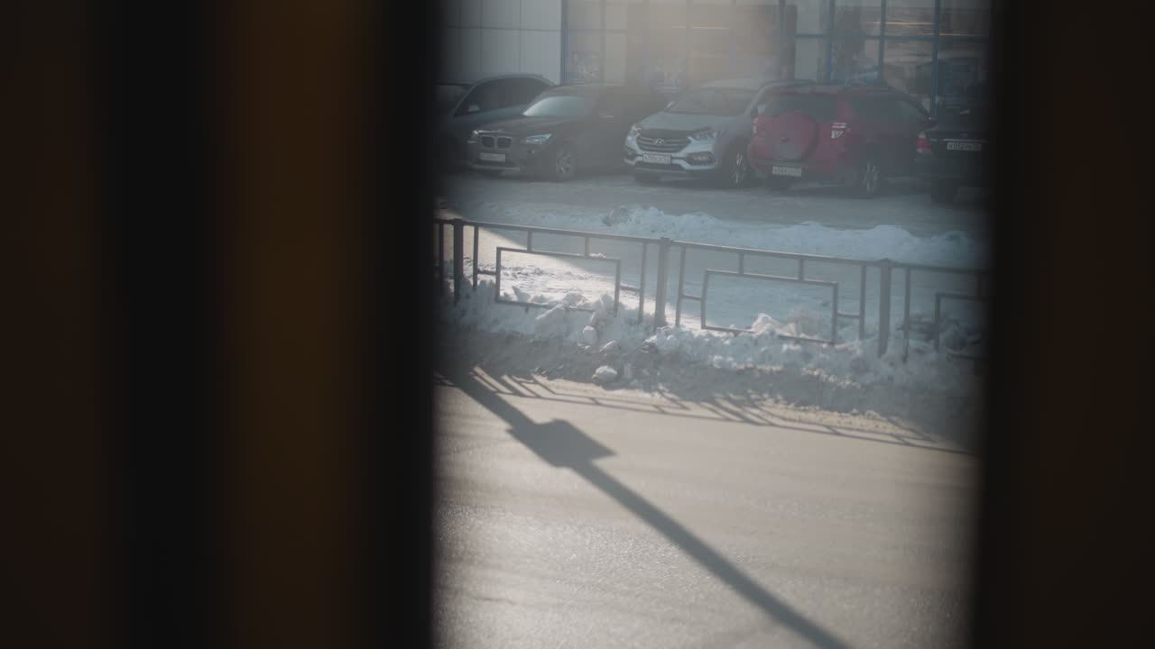 View through moving vehicle window shows people and cars on busy city road, soft blur from foggy glass, muted winter light, traffic queue near stop, distant silhouettes and gentle motion on asphalt