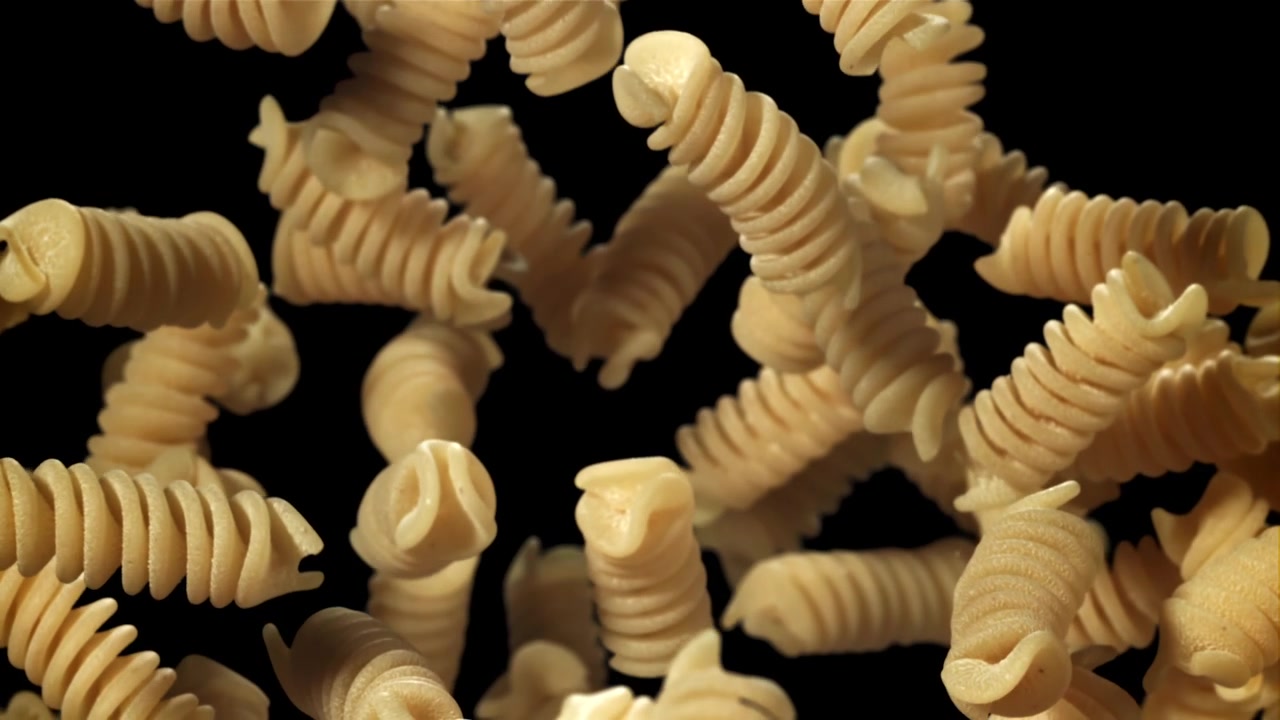 Fusilli crudi che cadono al rallentatore su uno sfondo nero