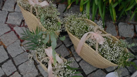 decorative baskets filled with baby's breath flowers and greenery, tied with pink ribbons, placed on a cobblestone path