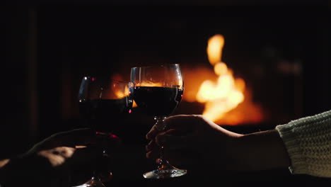 Vor-Dem-Hintergrund-Des-Kamins,-In-Dem-Das-Feuer-Brennt,-Gläser-Mit-Wein-Anstoßen