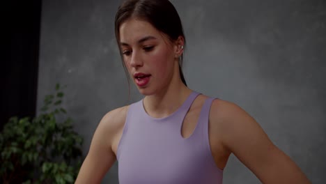 Confident-and-tired-brunette-girl-in-a-purple-sports-top-takes-a-deep-breath-and-exhales-after-doing-intense-sports-in-a-modern-apartment-at-home