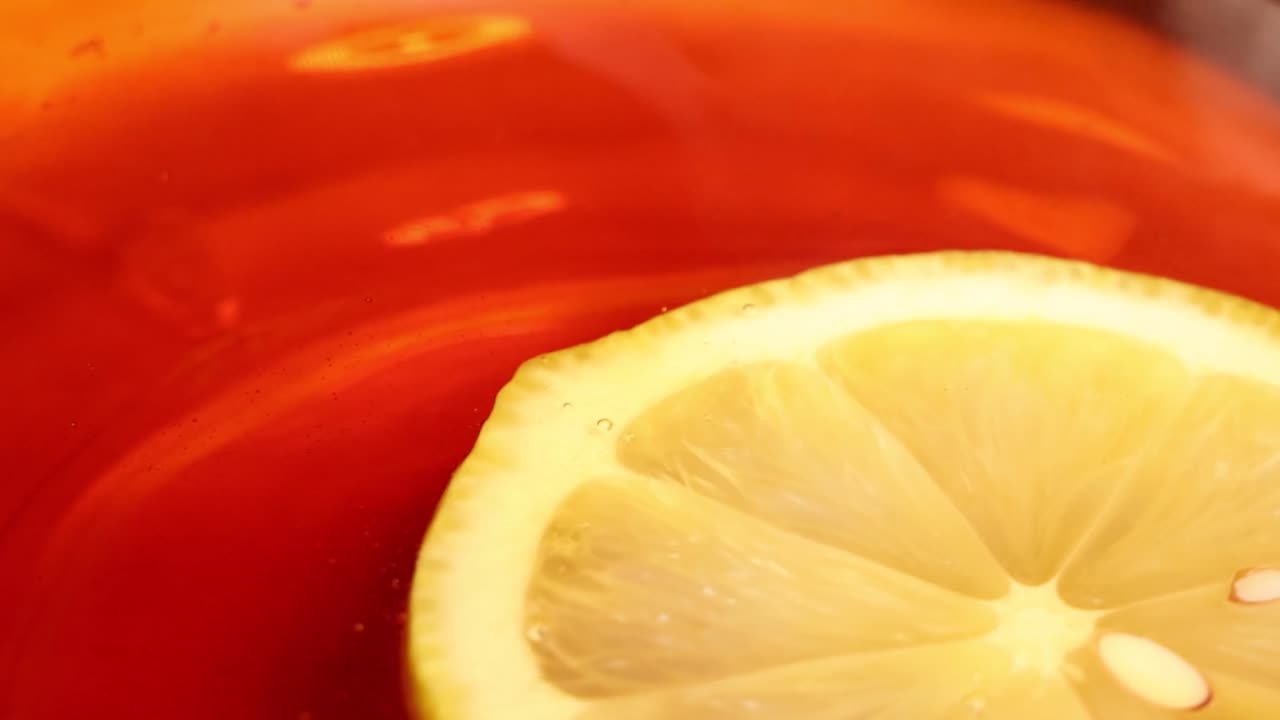 Vista macro di una fetta di limone fresco che cade nel tè, creando increspature e spruzzi dorati