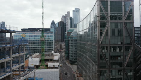 Forwards-fly-above-street-leading-between-multistorey-buildings.-Tower-cranes-on-construction-site-of-new-house.-Group-of-skyscrapers-ahead.-London,-UK