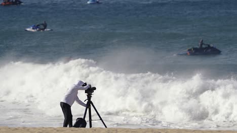 Kameramann-Am-Sandstrand,-Der-Surfer-Und-Jetskis-Auf-Großen-Wellen-Fotografiert