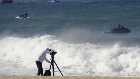 cameraman on sandy beach shooting surfers an jetskies on big waves