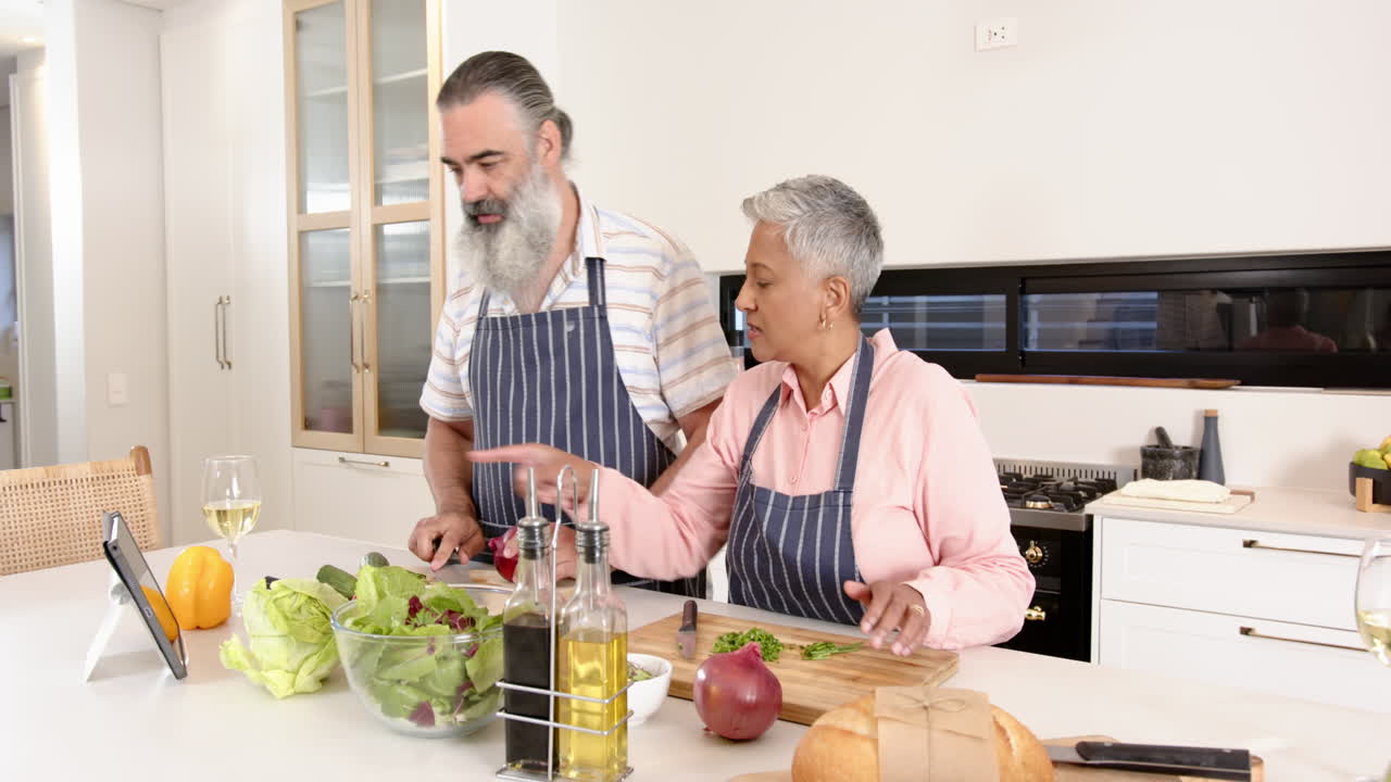 Preparing meal, senior couple following recipe on tablet in kitchen
