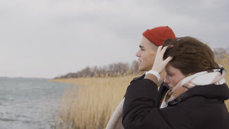 Side-View-Of-A-Teenage-Boy-And-Teenage-Girl-Talking-Standing-Near-Of-Seashore-On-A-Cloudy-Day,-Boy-Show-Something-With-His-Arm-1