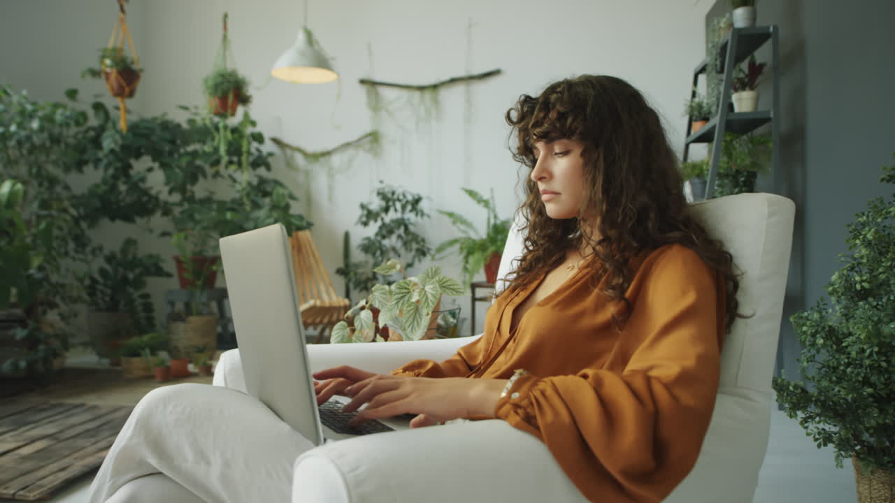 Woman Using Laptop in Room with Green Plants