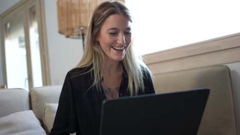 Tattooed-woman-celebrating-winning-money-working-with-a-laptop-on-the-sofa-of-her-house